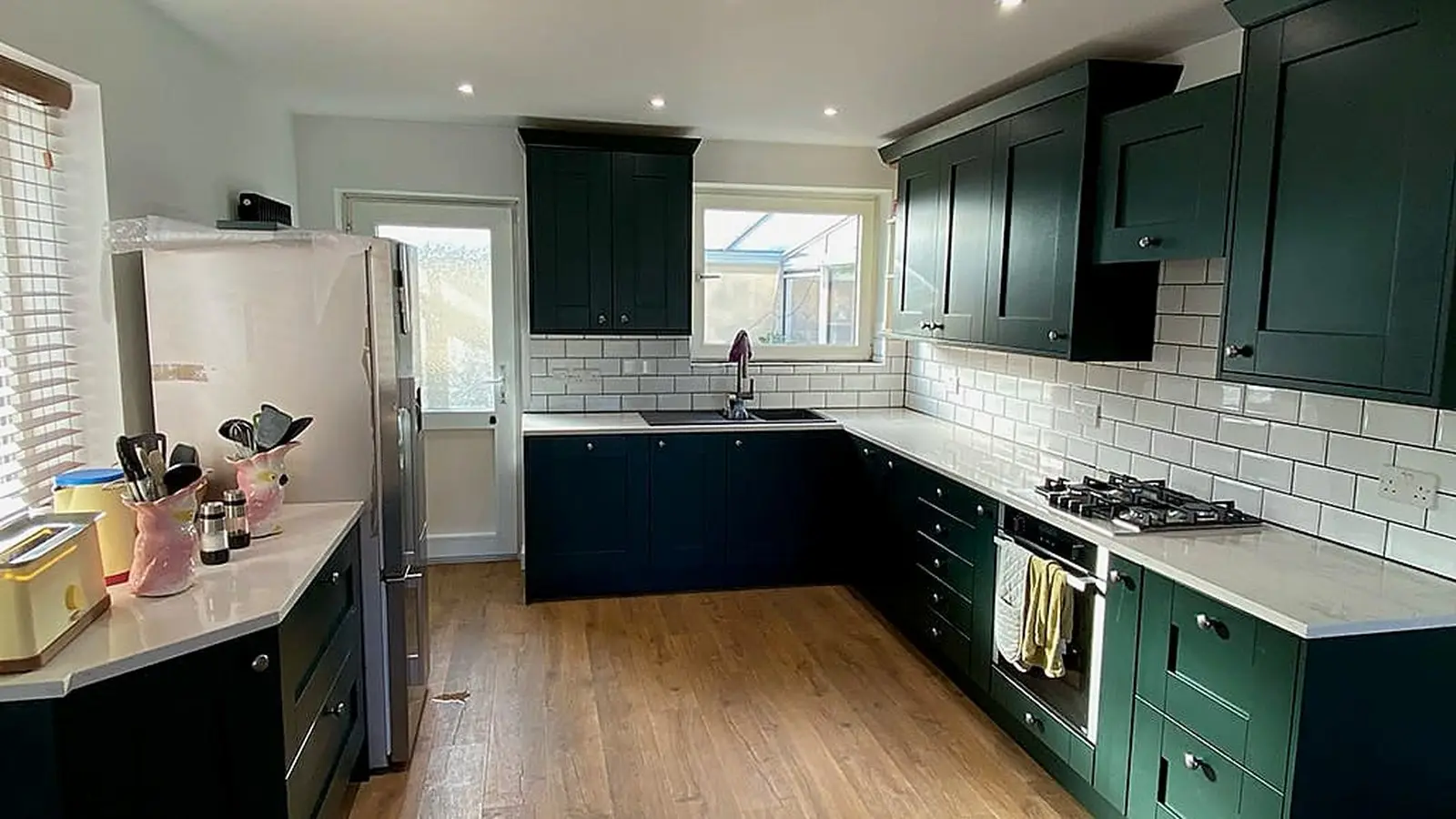 Finished kitchen extension in Bristol with dark green shaker units, white worktops and oak-effect flooring by Wilson & Cole