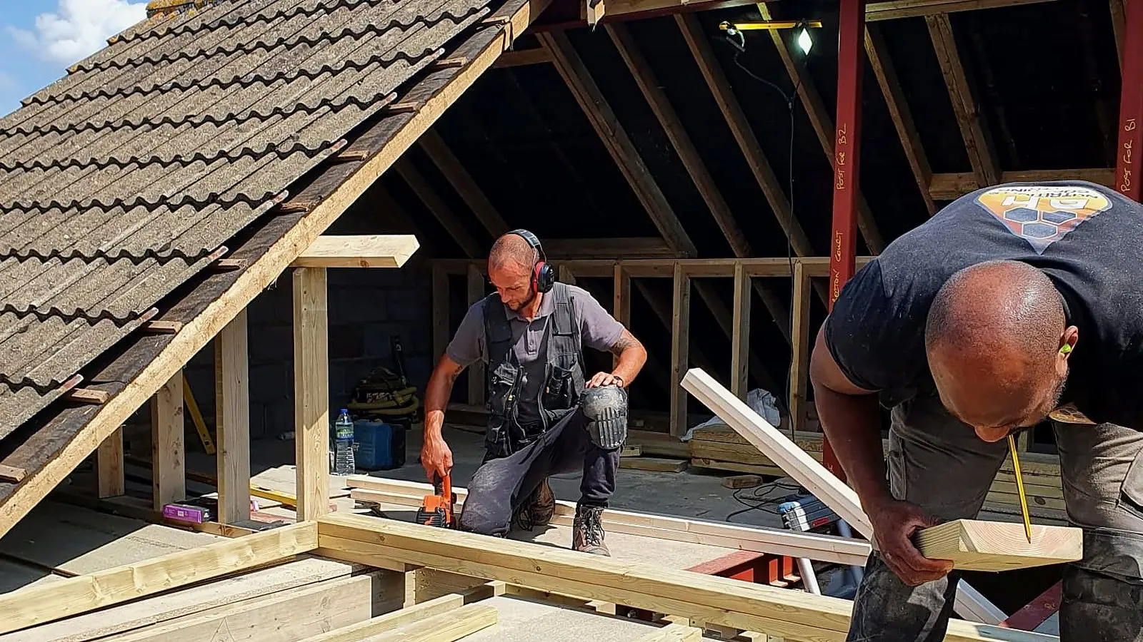 Two Wilson & Cole carpenters working on a new timber roof structure beside a pantile roof
