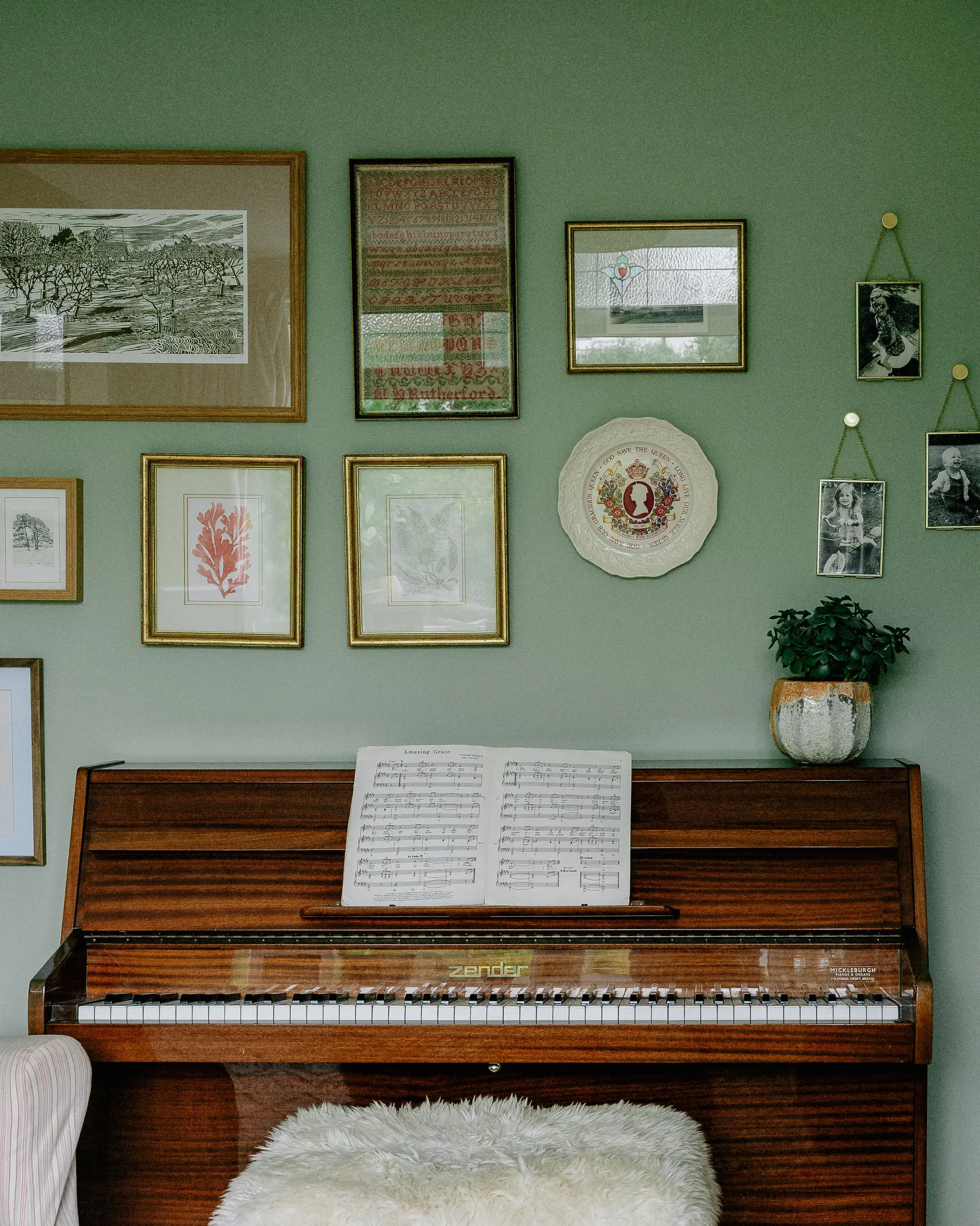 Living room painted soft green with a piano and framed prints